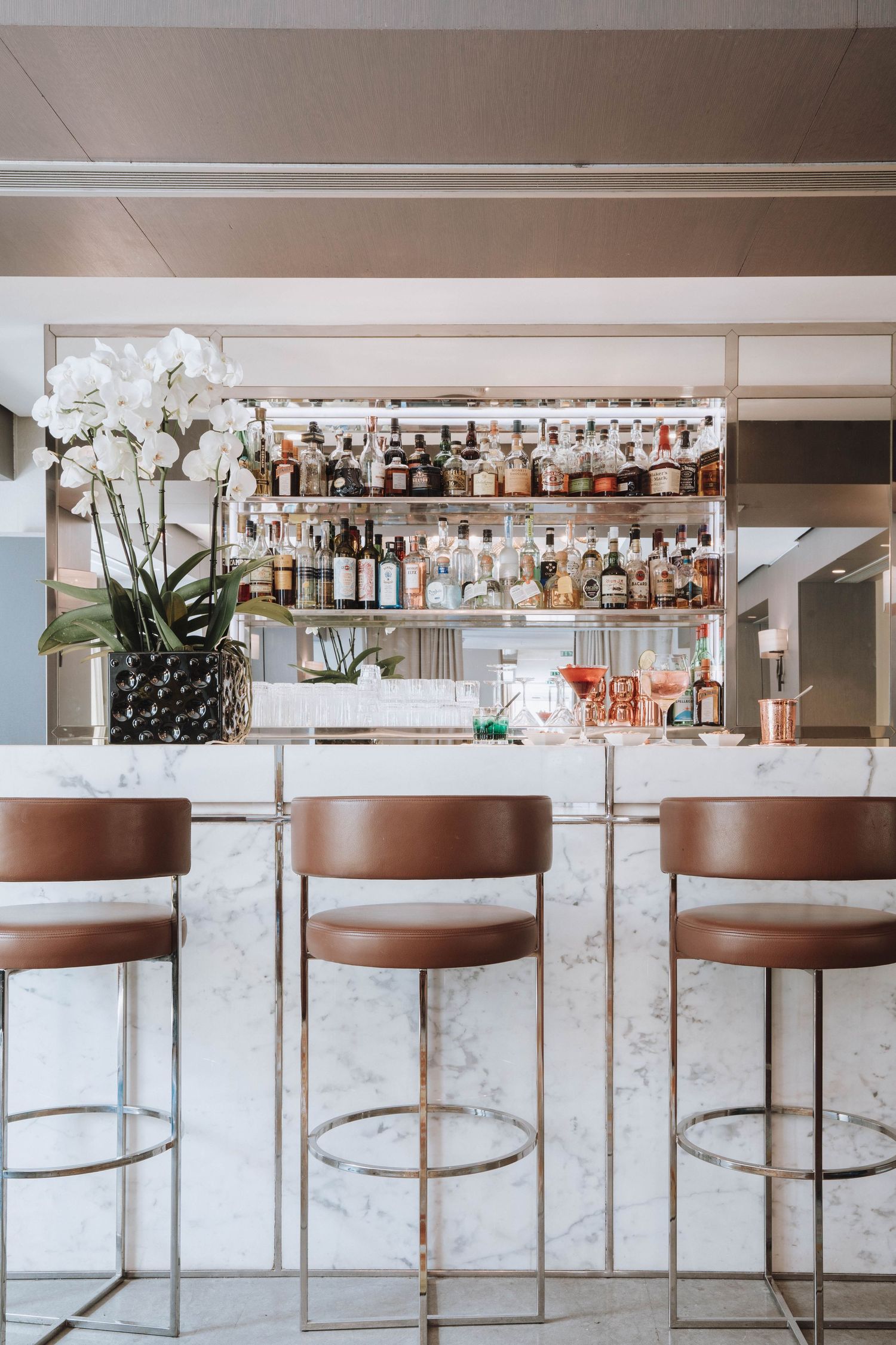 Elegant marble bar counter with brown leather barstools and white orchid display.