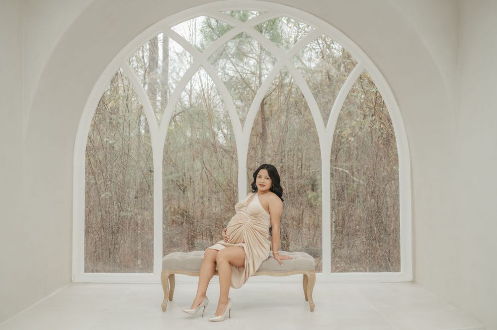 Woman in champagne dress poses elegantly on vintage bench in front of arched windows.