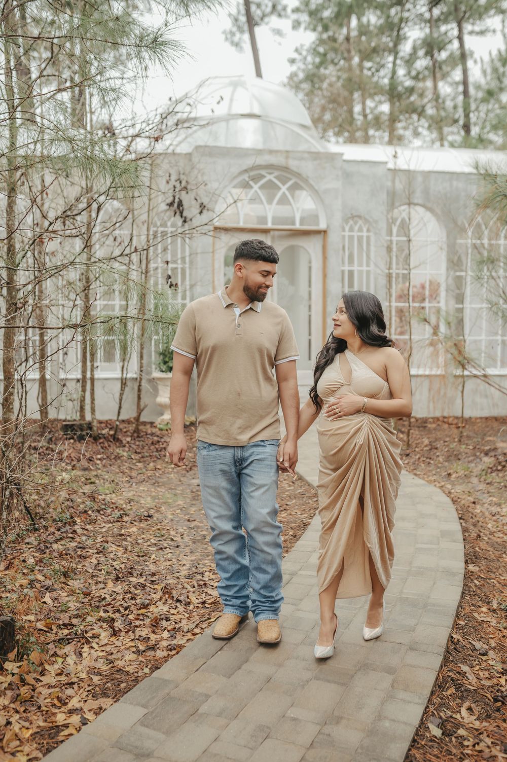 Couple strolls along garden path by white conservatory wearing coordinated beige outfits.