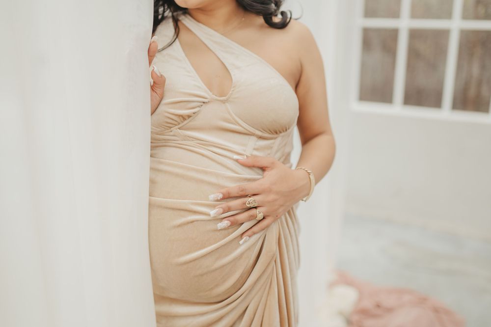 Close-up of champagne-colored draped dress details against white wall.
