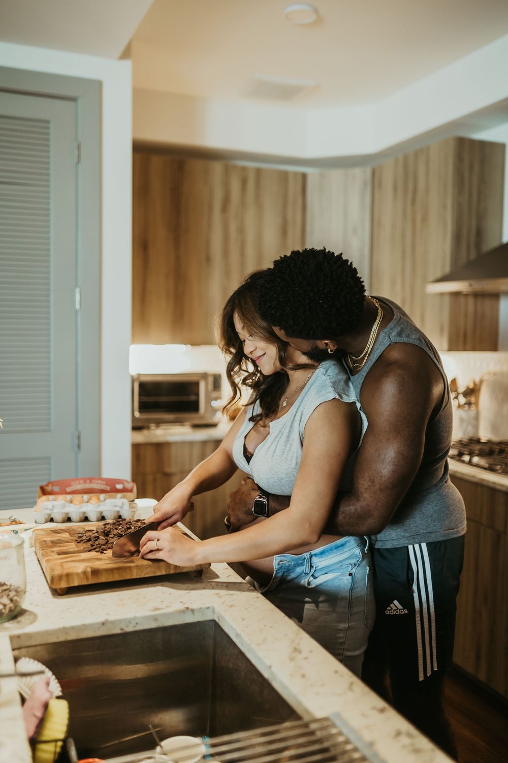 Couple preparing food together at kitchen counter with wooden cutting board.