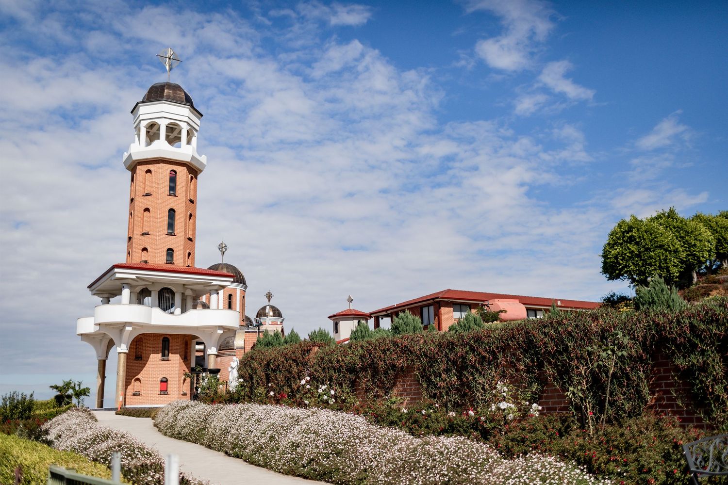 White lighthouse tower with red roof against blue sky in Mediterranean setting.
