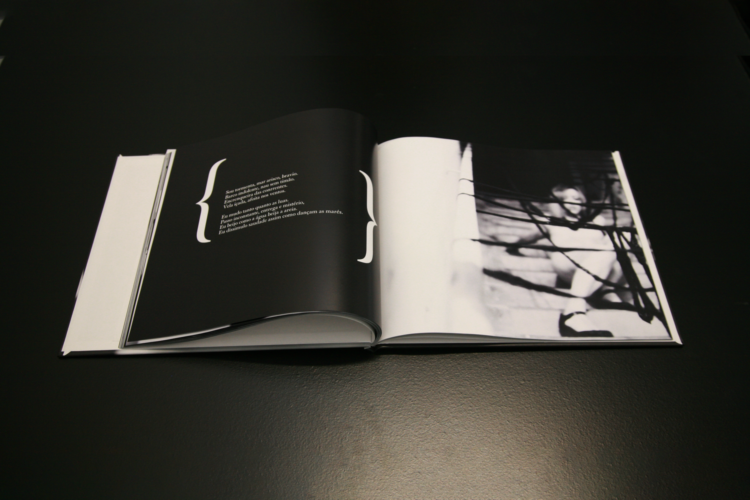An open photography book displays black and white images and text on matte pages under dramatic lighting.