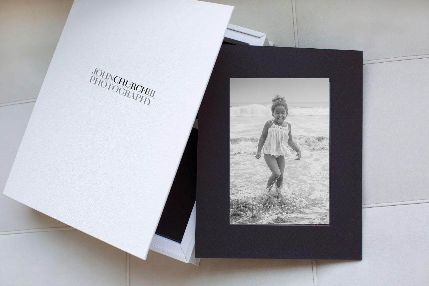Black and white photo of a child playing at beach displayed in white photography presentation box.