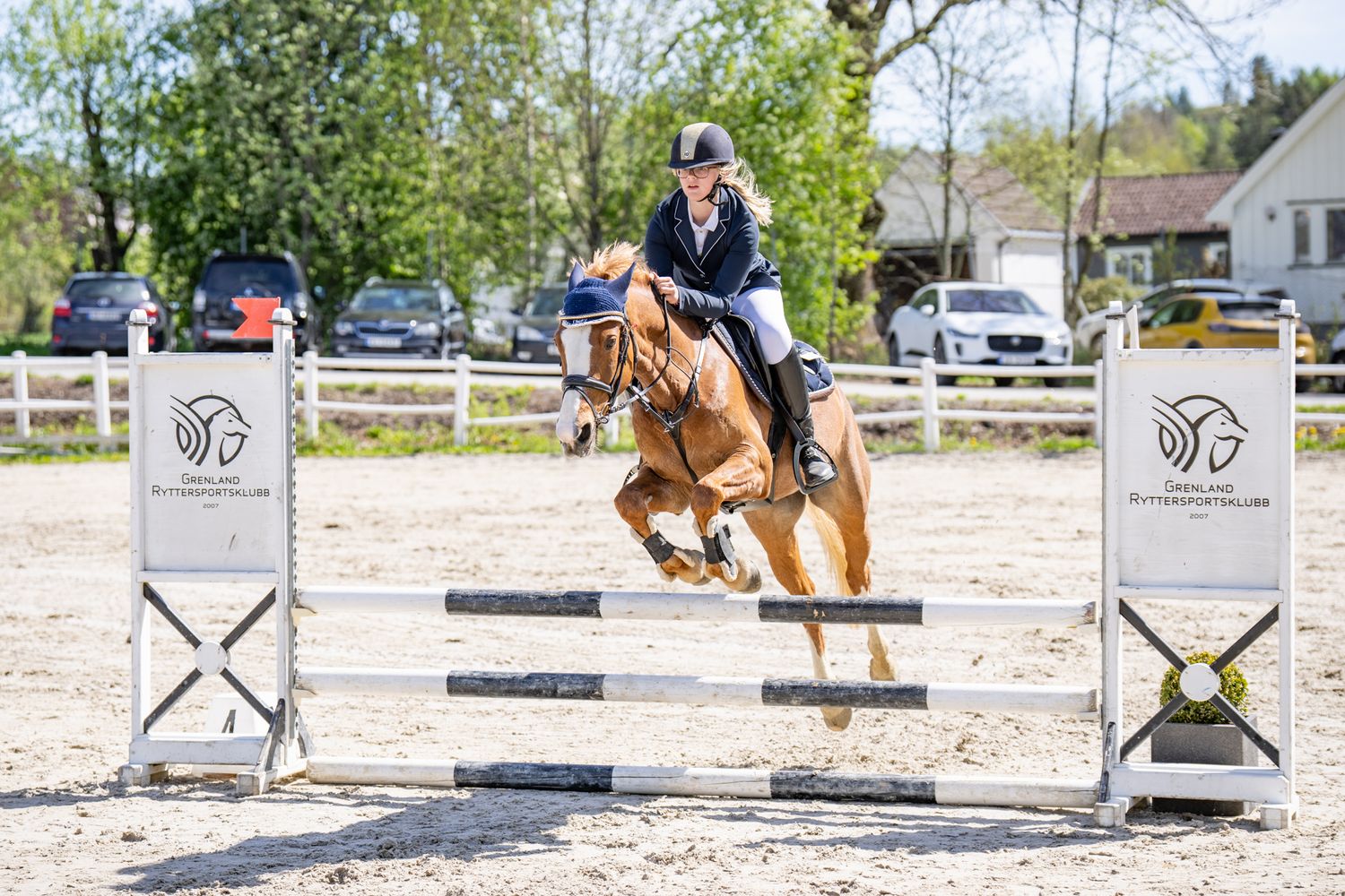 Horse and rider clearing numbered jump between white posts in competition ring.