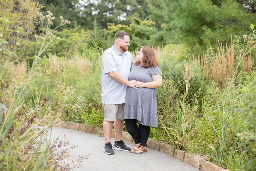 two adults hugging with hands on woman's belly on a path through greenery at longwood gardens pennsylvania