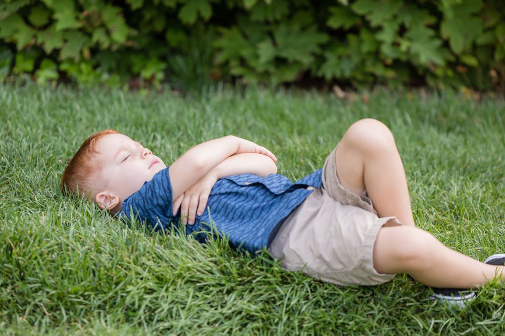 redheaded boy laying in grass pretending to sleep in Longwood gardens Pennsylvania for a pregnancy announcement session