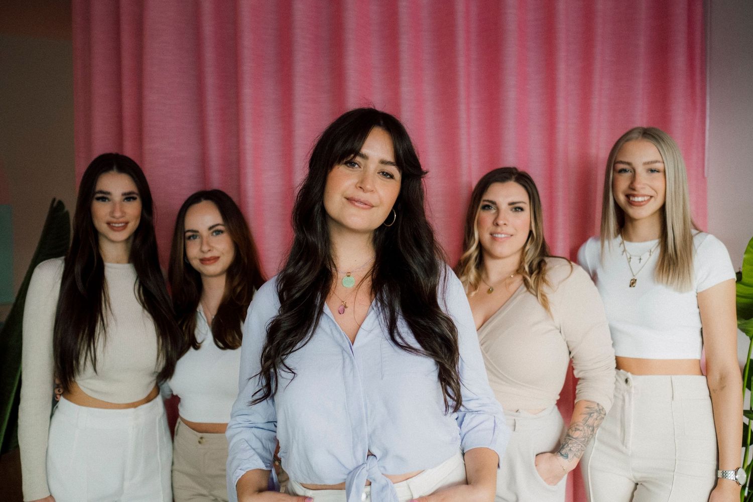 Group photo in matching white and neutral outfits against pink curtain backdrop.