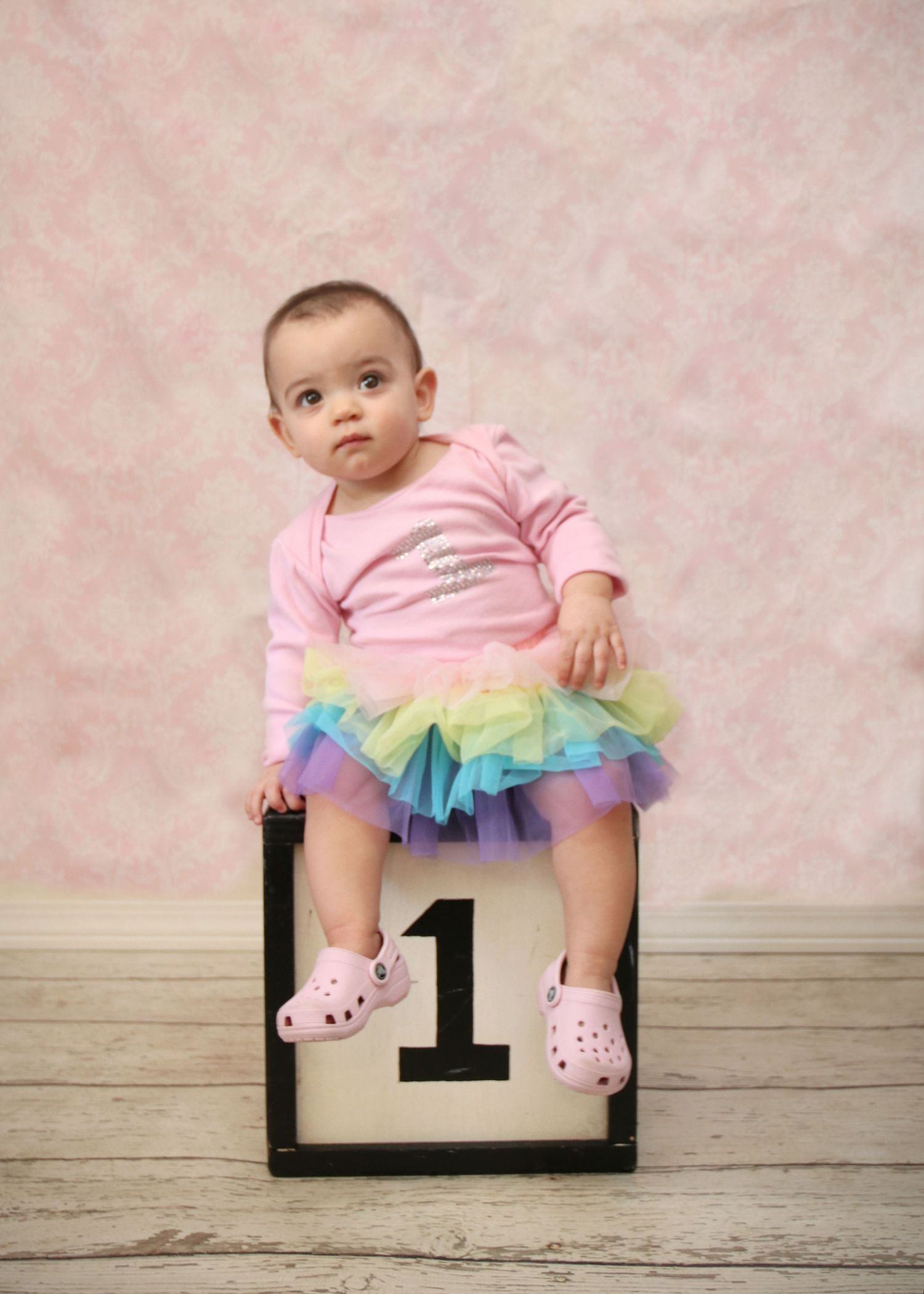 First birthday portrait on wooden box with rainbow tutu and pink outfit.