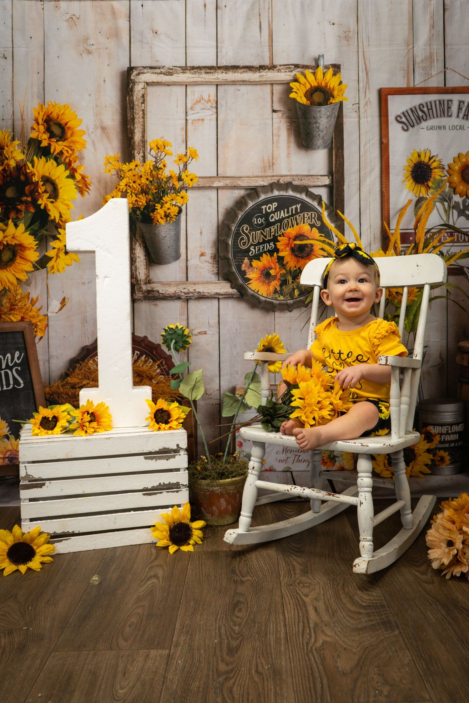 Rustic sunflower themed photography setup with white rocking chair and number one decoration.