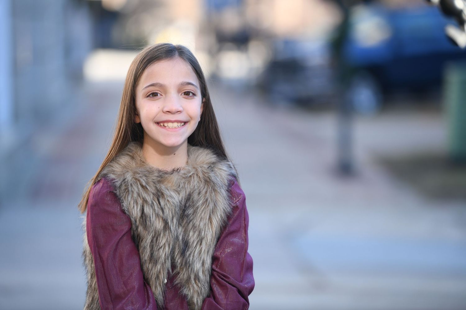 Outdoor portrait with burgundy sweater and fur vest showing warm smile.