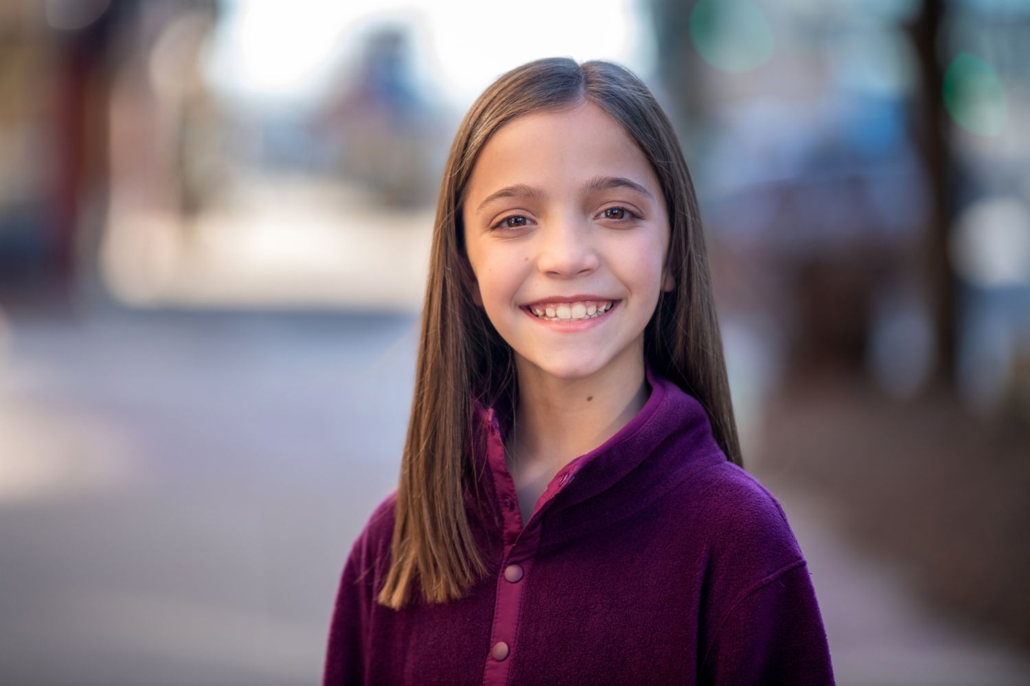 Bright outdoor portrait showing cheerful expression in purple fleece jacket.