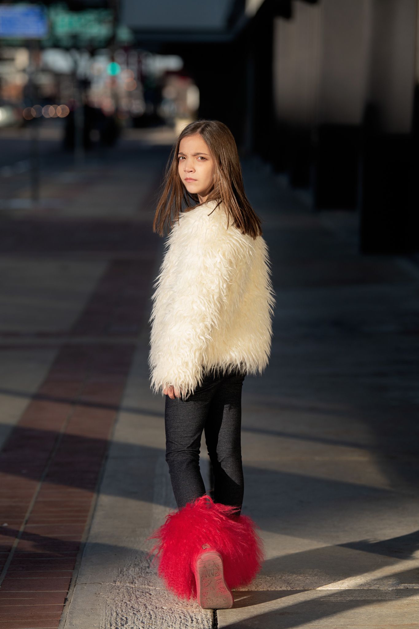 Street fashion portrait with white fuzzy coat and red boots in urban setting.