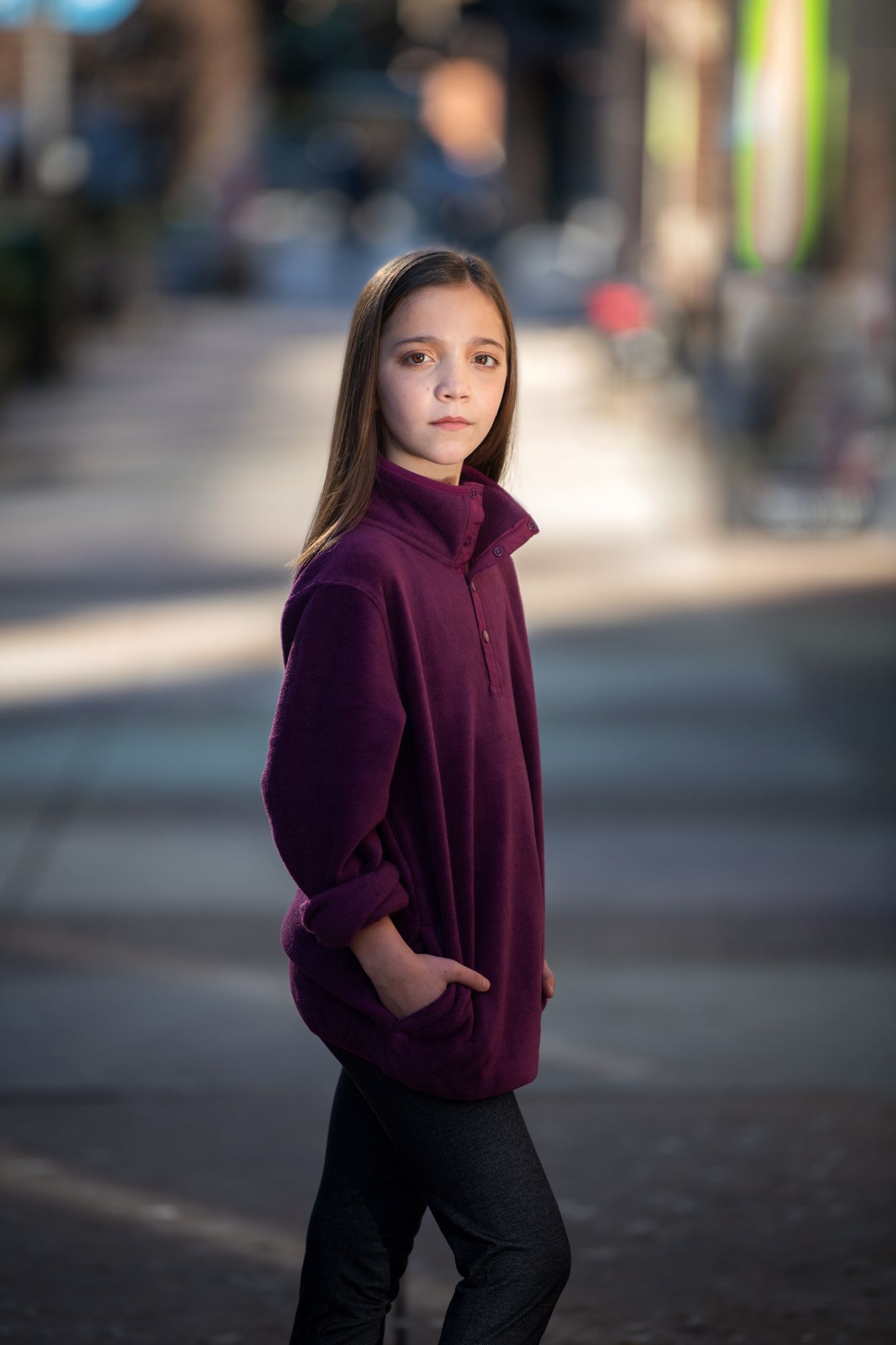 A person wearing a burgundy fleece jacket poses on a city street with blurred background.