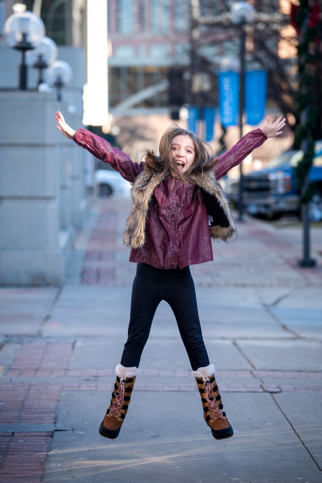 An energetic jump shot on a city sidewalk wearing winter boots and burgundy top.
