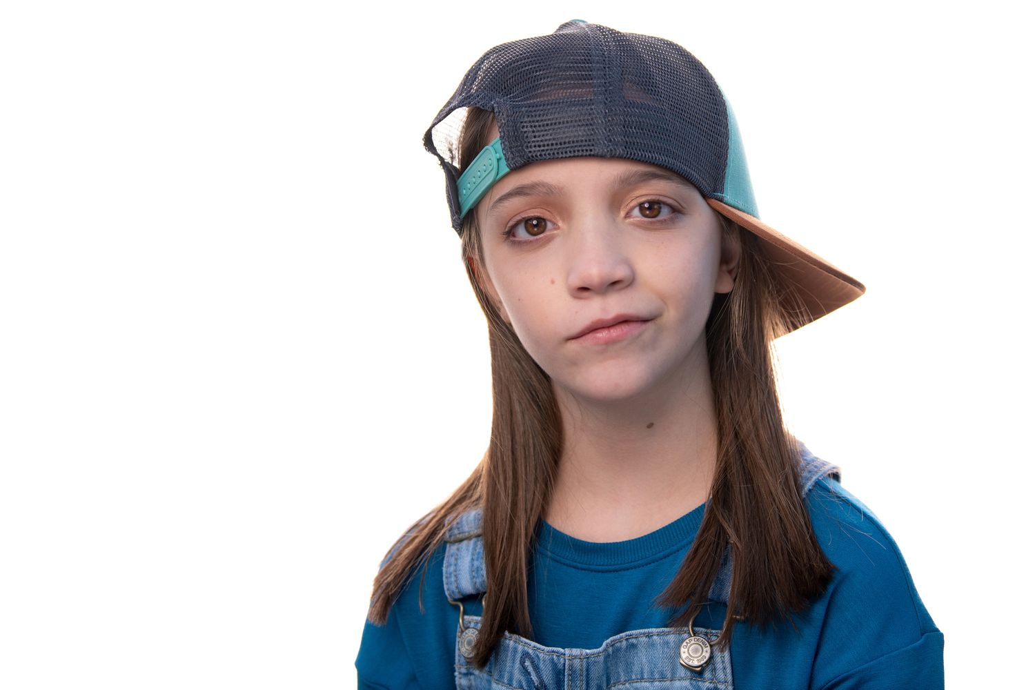 Studio portrait with baseball cap and denim overalls against white background.