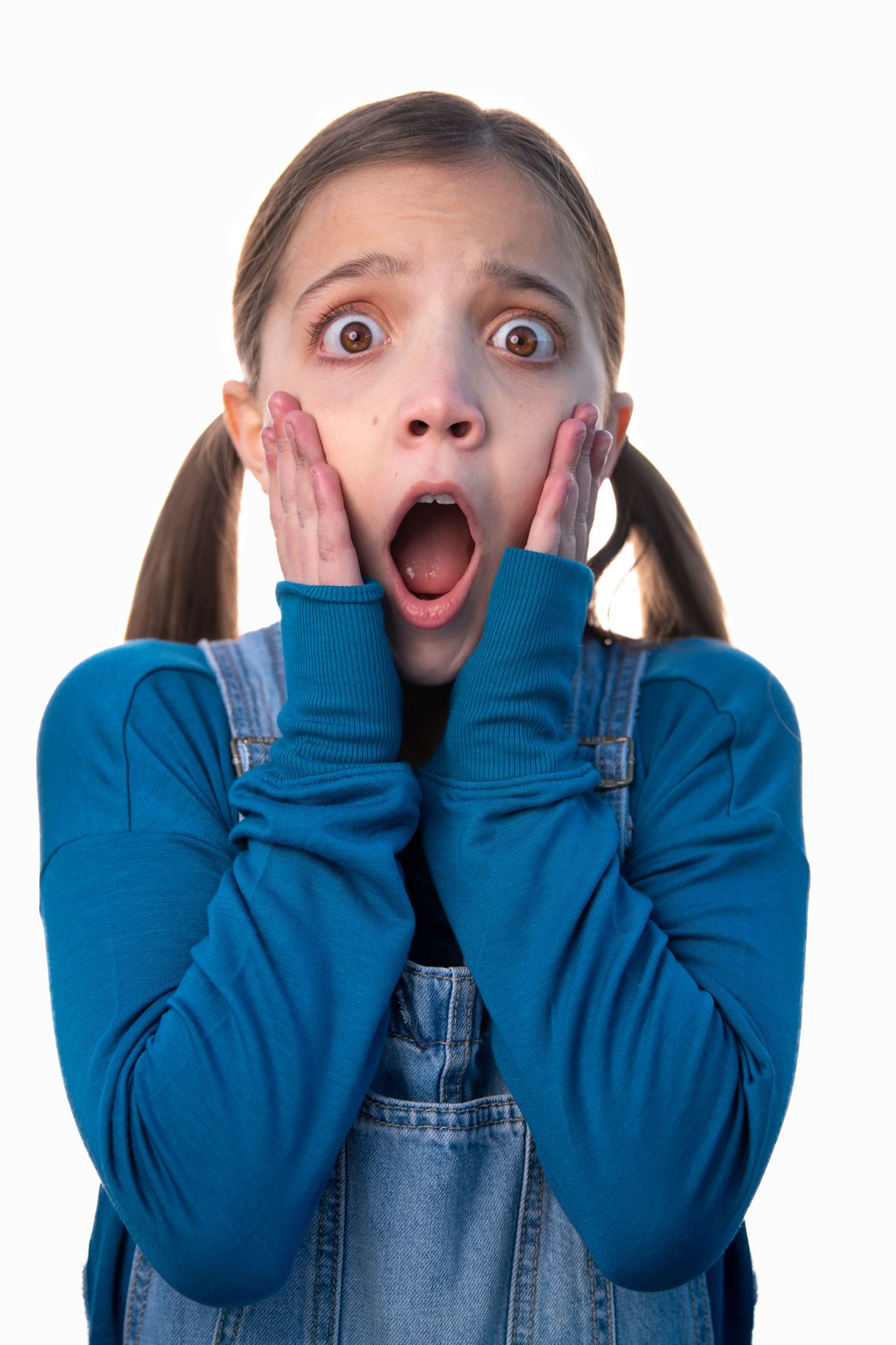 Portrait of an expressive figure in blue sweater and denim overalls showing shock with hands on cheeks.