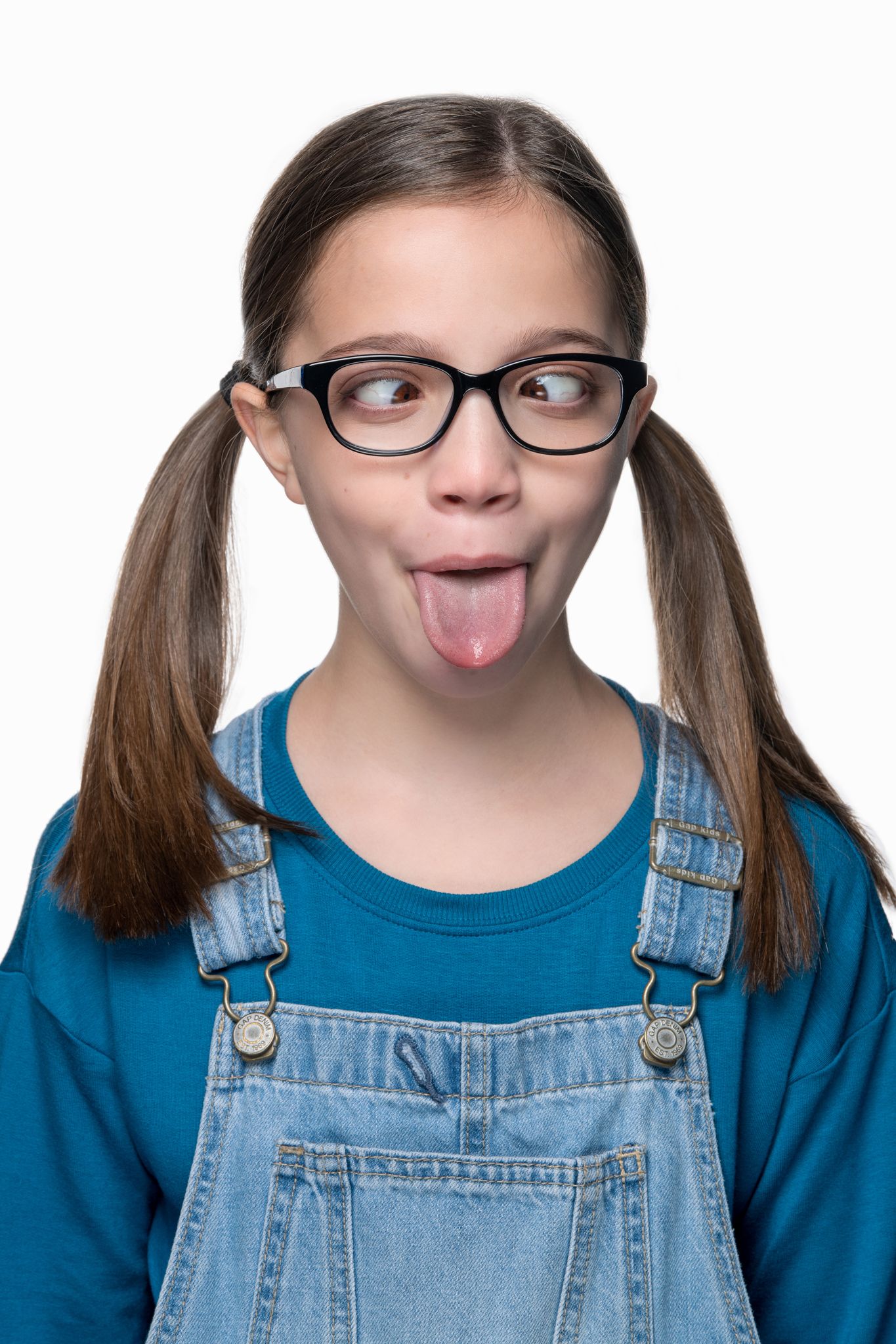 Playful portrait showing crossed eyes and tongue out while wearing glasses and denim overalls.