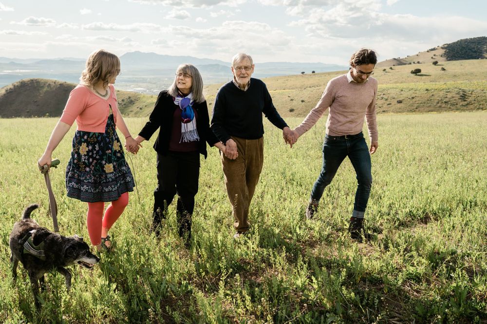 A group walks hand in hand through a grassy meadow with their dog on a sunny day.