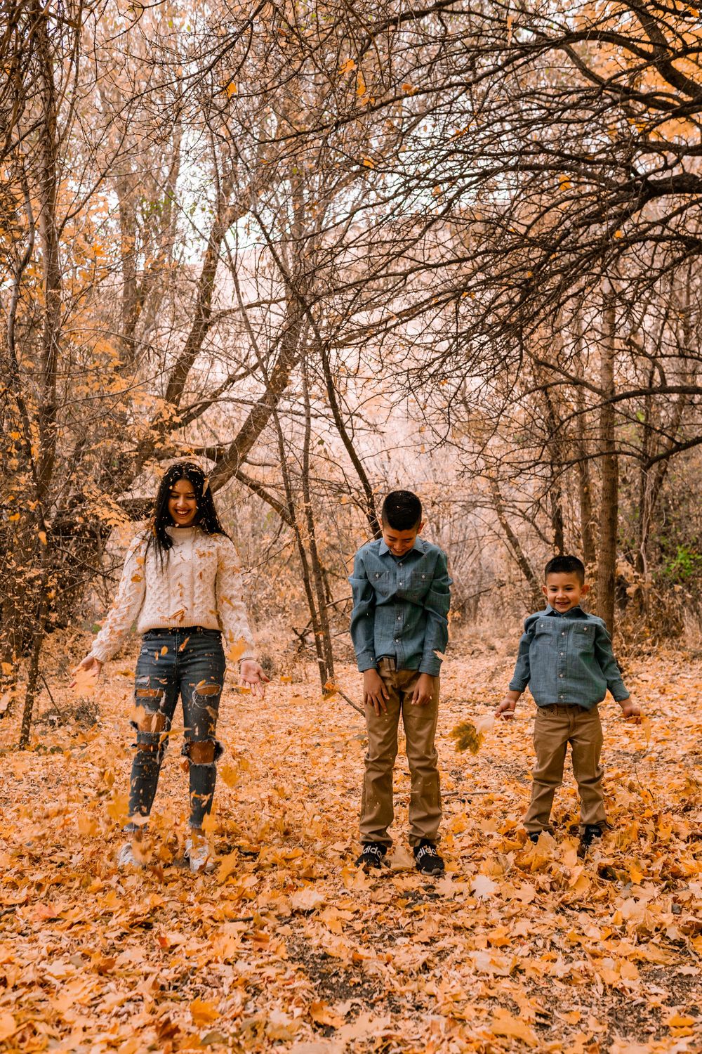 Three people jump playfully among fallen autumn leaves in a forest setting.