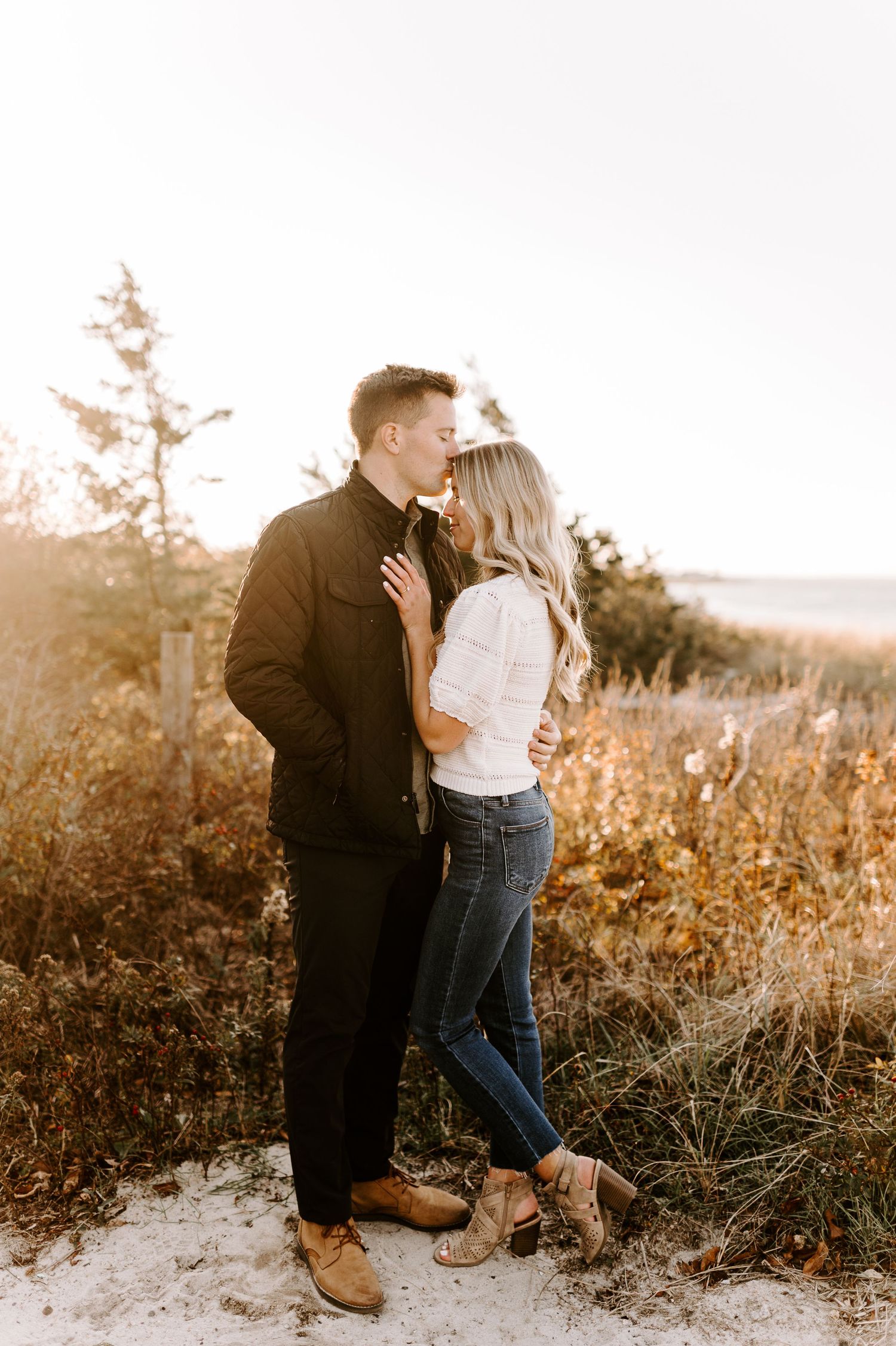 Couple sharing tender moment on sandy beach path during golden hour.