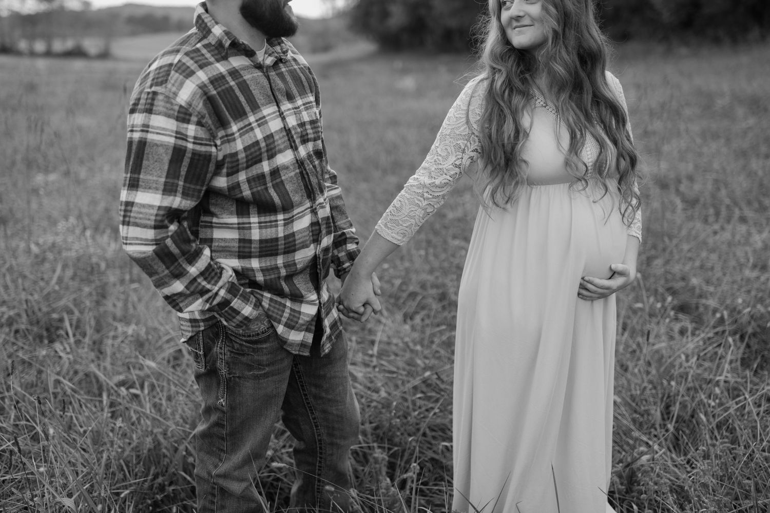 A romantic couple standing close in a field during golden hour.