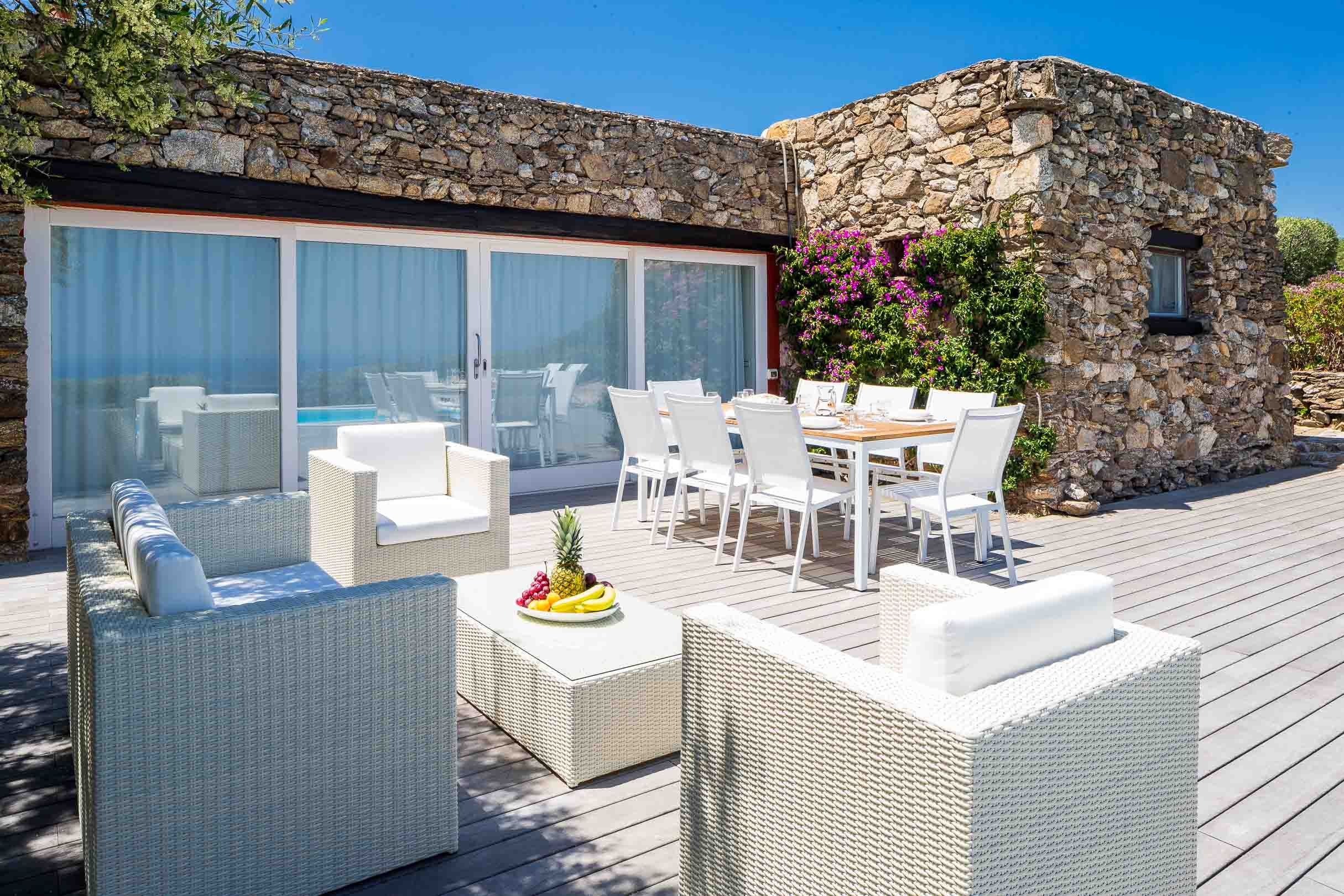 Stone villa terrace with modern white outdoor furniture and glass windbreak panels.