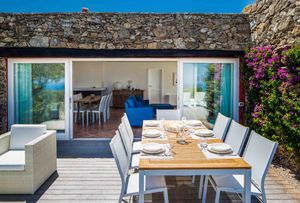 Modern stone villa with sliding glass doors opening to outdoor dining area and sea views.