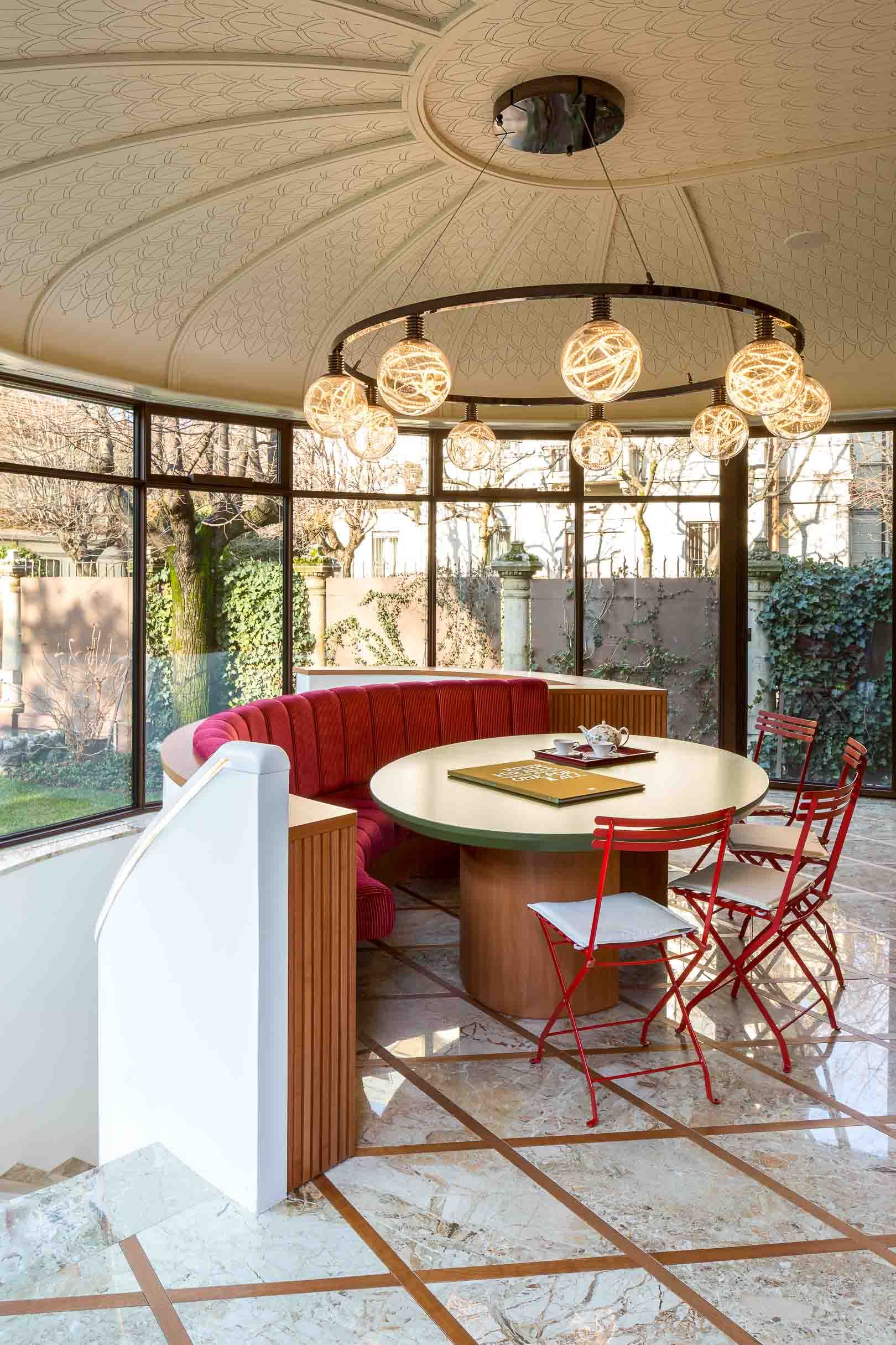 Circular sunroom with curved red banquette seating and decorative pendant lights under domed ceiling.