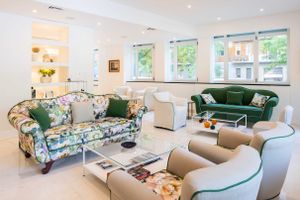 Bright living room with floral patterned sofa, green velvet couch, and white accent chairs.