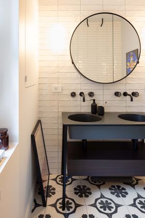 Modern bathroom with round mirror, black vanity, and geometric patterned floor tiles.