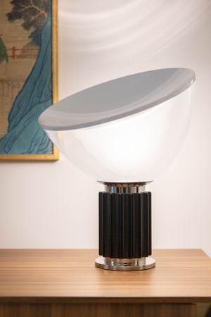 Modern table lamp with white dome shade and black ribbed base beside Asian-inspired artwork.
