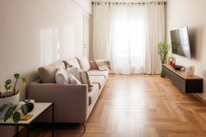 Bright living room with gray sofa, herringbone floors, and sheer curtains.