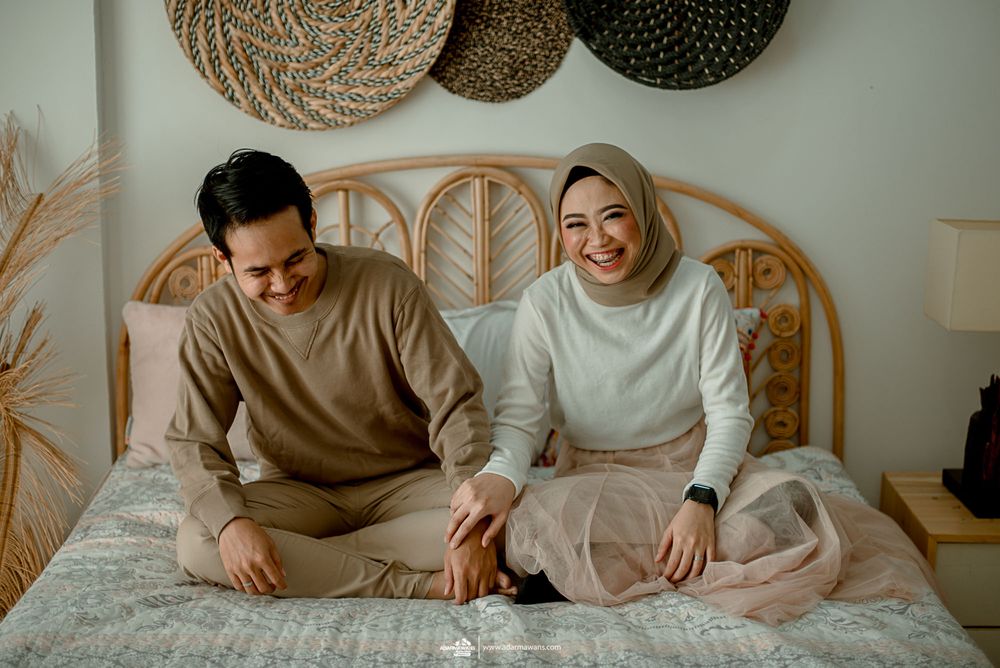 Casual couple sharing a moment on bed beneath woven wall decor.