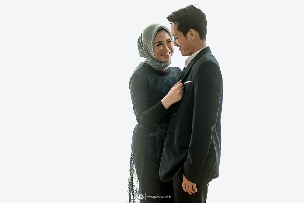 A romantic couple in formal attire poses intimately against a light background.
