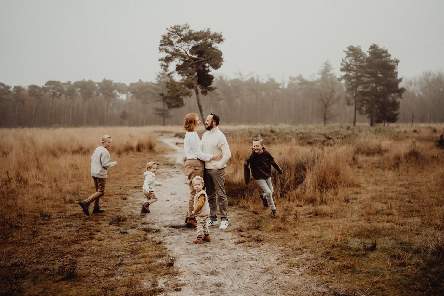 Family running and playing together on a dirt path through a misty autumn field.
