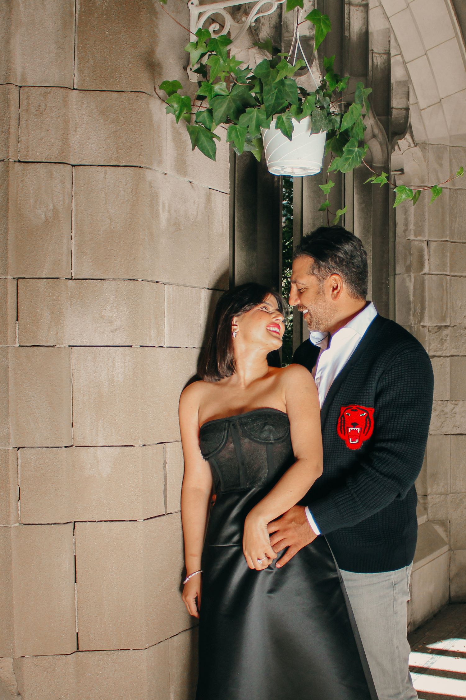 A couple sharing an intimate moment under a hanging plant in an elegant stone corridor.