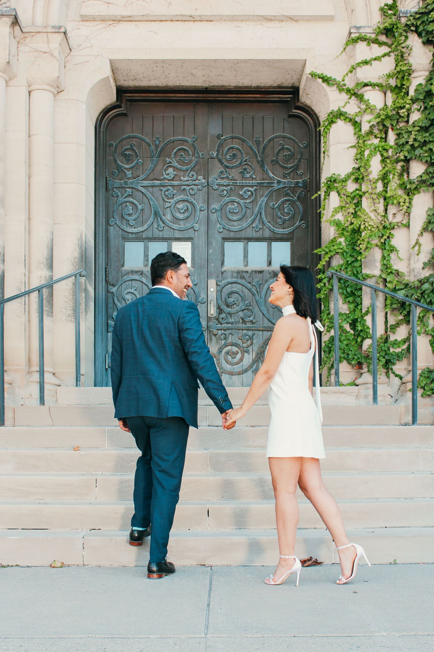 A couple walking up stone steps towards an ornate church door with decorative ironwork.