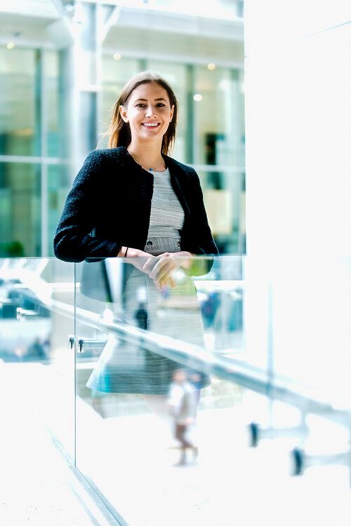 Professional in business attire smiling at modern office building with glass railings.