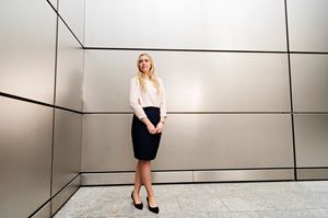 Professional in business attire standing against geometric wall panels in modern interior.