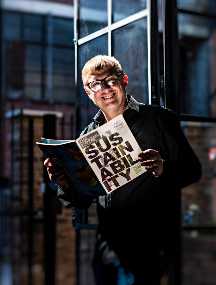 Young person in black jacket reading a newspaper by a window.