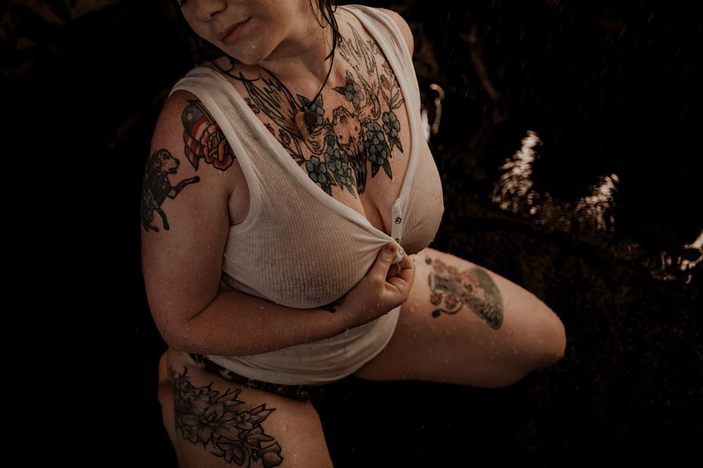 Artistic boudoir photo with moody lighting and dark background showing a figure in intimate pose.