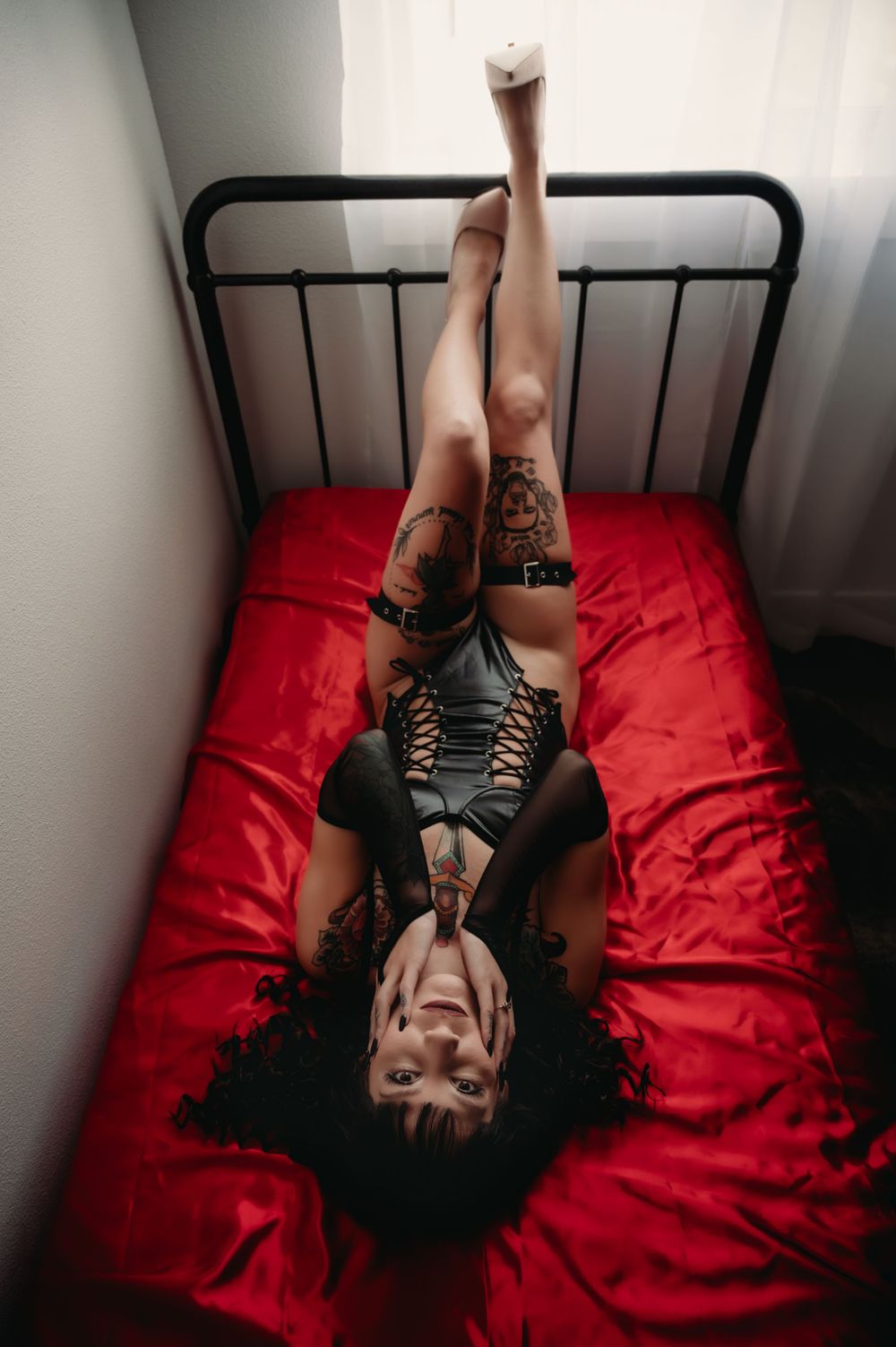 Dramatic overhead view of figure reclining on red bedding with black metal headboard.