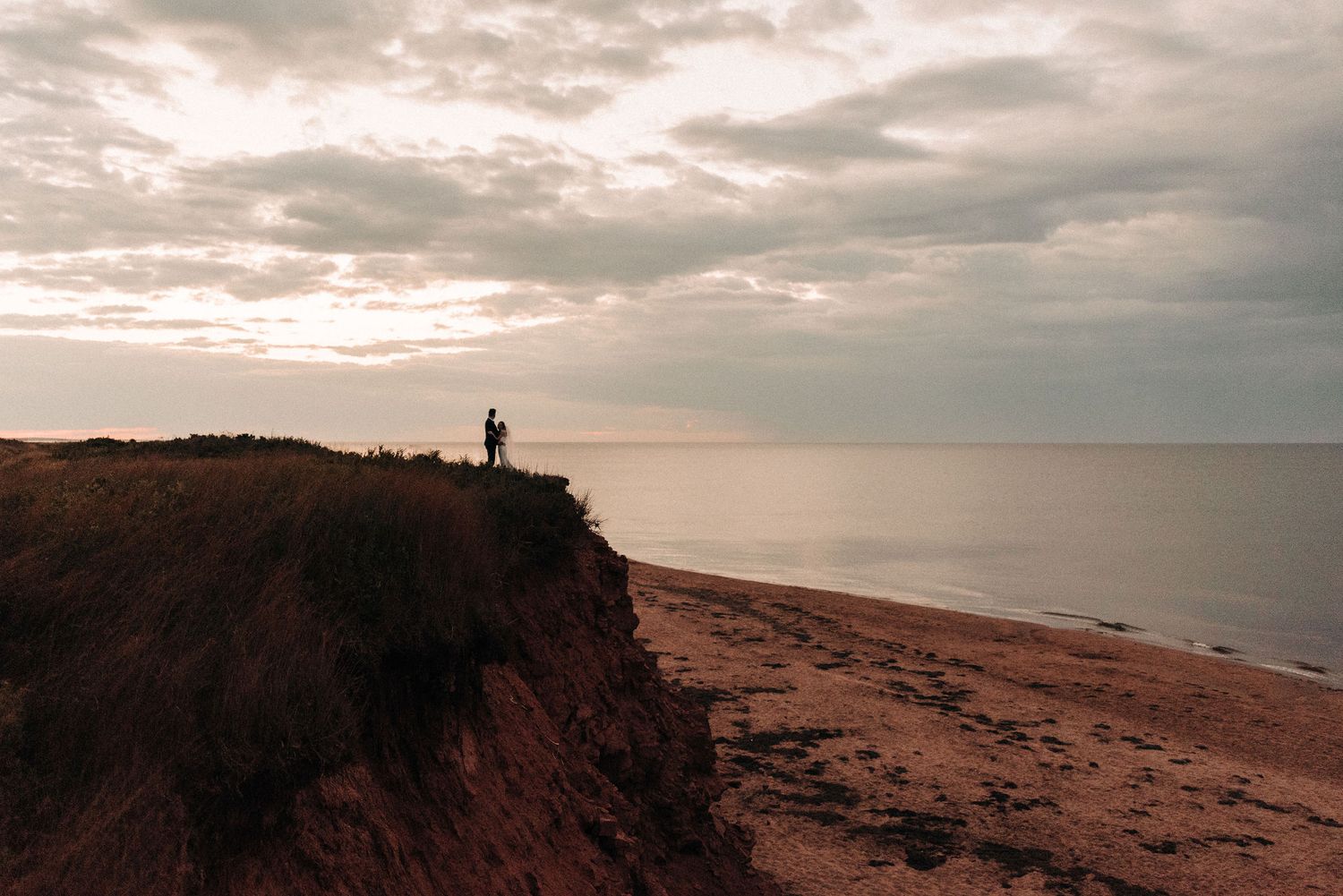 Silhouette on coastal cliff edge overlooking ocean under moody sunset sky.