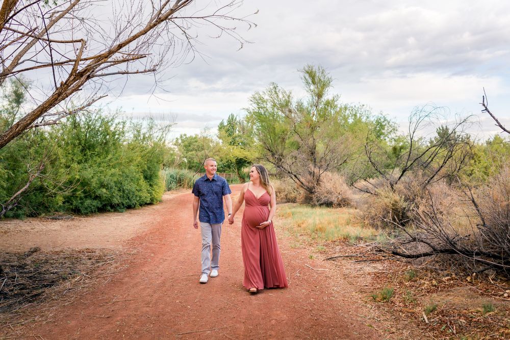 Couple walking on red dirt path surrounded by desert vegetation.