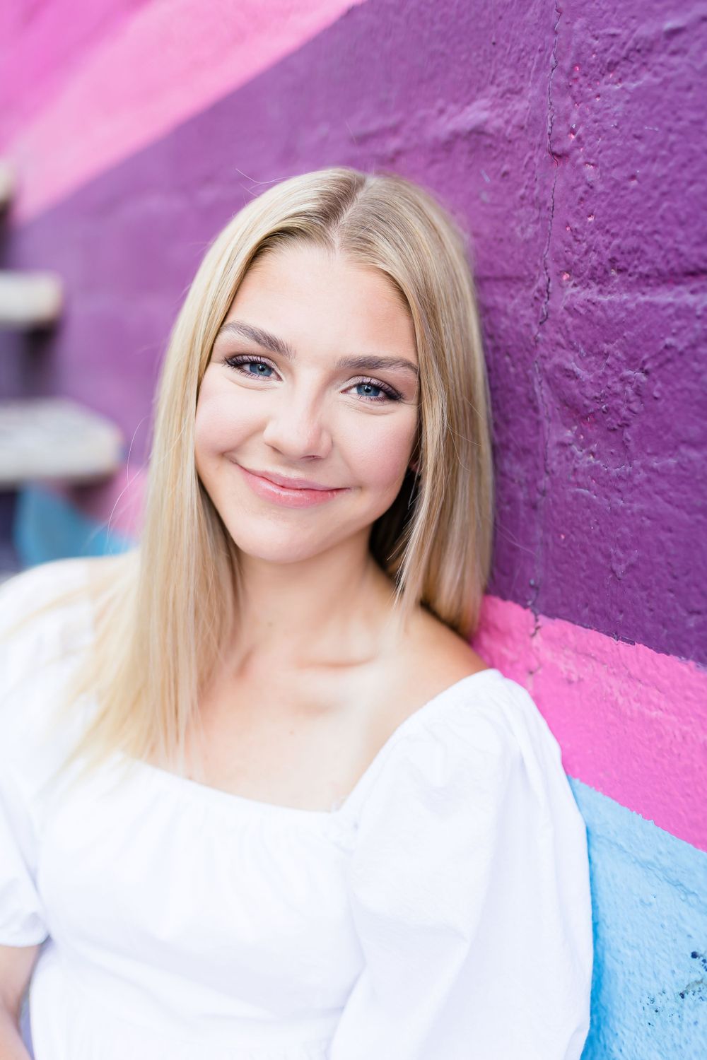 Portrait against colorful painted wall wearing white top.