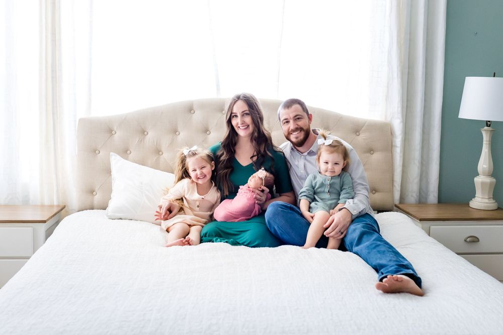 Family relaxing together on a cozy white bed in a bright bedroom with teal walls.