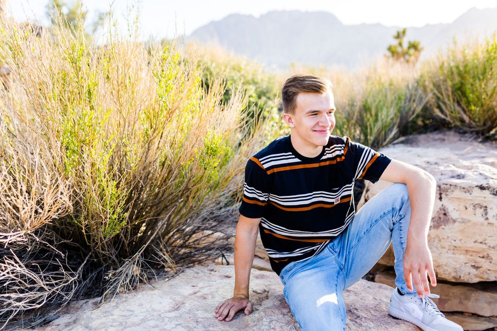 Young man in striped shirt sitting casually in desert landscape setting.