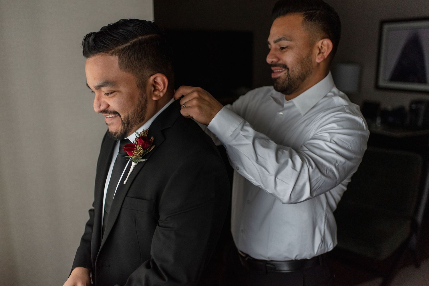 A groomsman helps adjust another's formal black tie and boutonniere before the wedding ceremony.