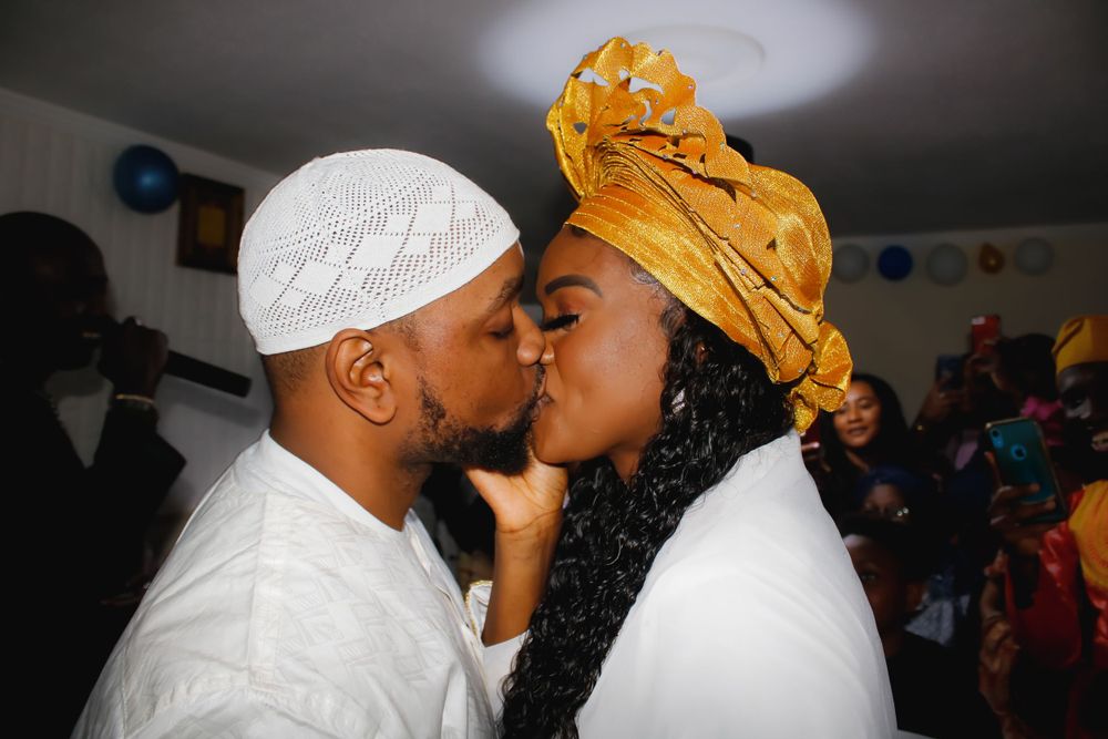 Romantic kiss between couple wearing white and gold traditional headwear.